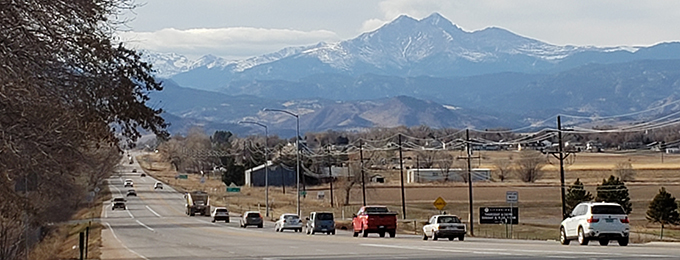 Multiple cars drive on state highway 66 with a view of Longs Peak in the background