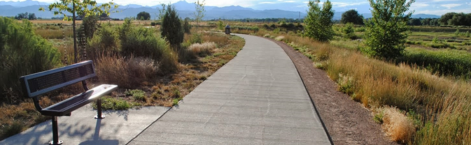 A metal bench is seen along a greenway in an open space area in Longmont