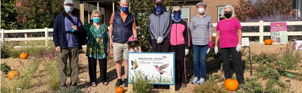 Community volunteers pose in front of the "Pollinator Garden" sign