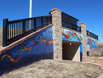 Pedestrian underpass tunnel face, painted with variegated blues and a rainbow tree trunk and branches.