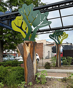 two stumps decorated with abstract tree canopies and bike chain details at the base are shown in an alley.