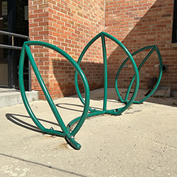 a picture of a bike rack that also looks like simple green leaves sticking up from the ground. it is in front of a brick building.