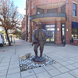 a bronze sculpture of the american president Roosevelt is pictured in front of a building bearing his name with concrete sidewalk surrounding him.