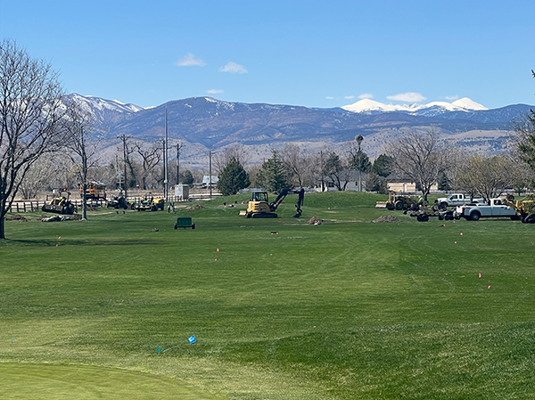 Mountains are visible behind a golf course that has some yellow digging machines on it.