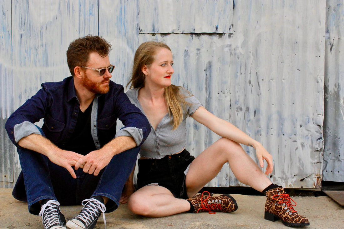 Bonnie&Taylor sitting outside in front or a corrugated wall