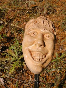 a photo of a ceramic face grimacing with open eyes and wrinkles. The background is of grass and the face is held up by a metal stick.