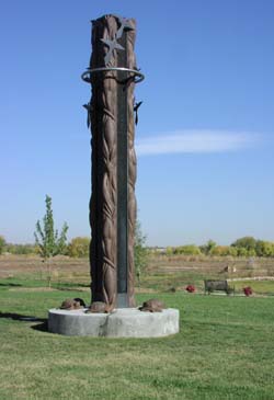 a tall tower is shown standing out in a grassy field. The tower has turtle sculptures at its concrete base and swirling pipes surrounding the tower to the top.