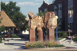 an image of a brick sculpture is seen in a park with trees and flowers planted with a blue sky