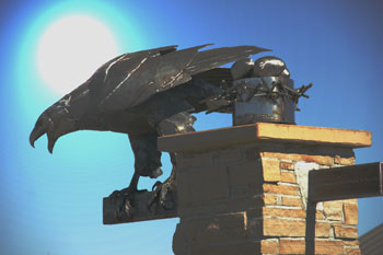 a metal welded eagle sits on a brick column in a photograph with a sunburst behind it