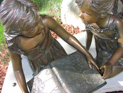 a close up photograph of a sculpture of two young people holding a book between them.