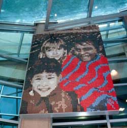 an image of a square tile mosaic inside a building shows a pixelated image of 3 children embracing