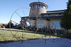 an image of a bike rack outside of the longmont recreation center is shown. The rack is a funky design that resembles a bike with many wheels.