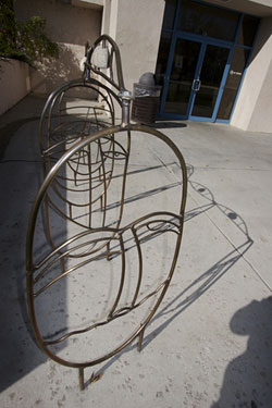 a photo of a bike rack with whimsical faces is shown next to the entrance of a building with blue doors. The shadows of the bike rack show eyes on the concrete.