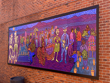 Mural on a brick wall. Mural features people and human skeletons in a cemetery painted mostly in purples and blues.