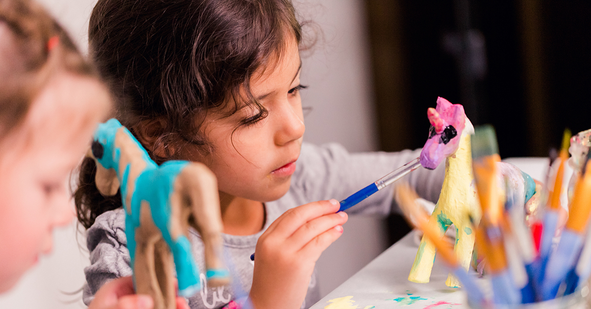 Little girls decorating small paper mache unicorn figurines.