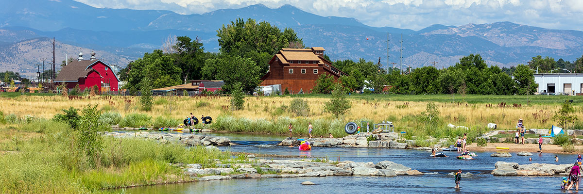 This photo of Dickens Farm, used Courtesy of Confluent Design, shows people using tubes in the St. Vrain creek with snow capped mountains in the background.