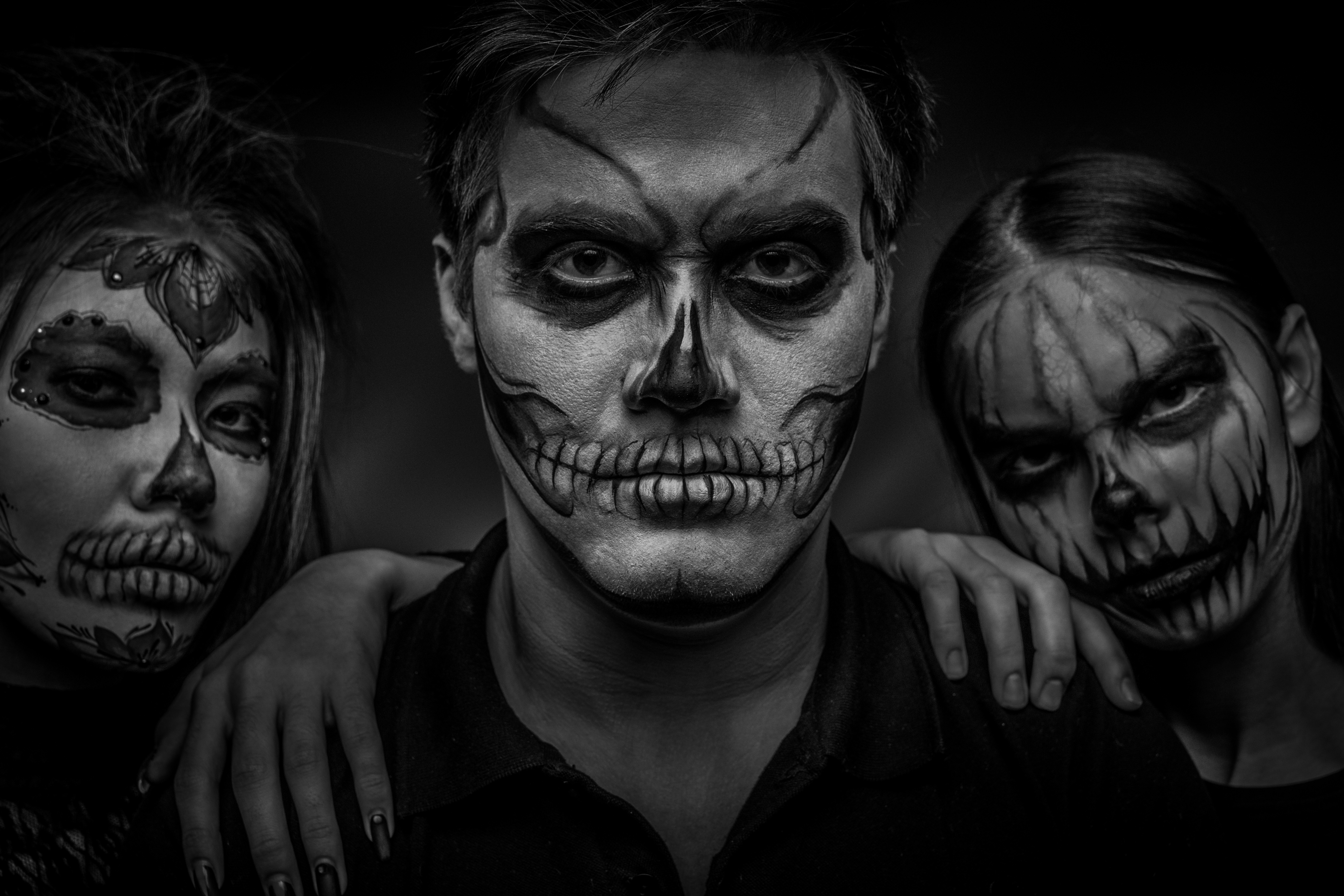 Male and female face art for Halloween. Black and white portrait of a guy and two girls with scary painted faces on a black background. All saints ' night.