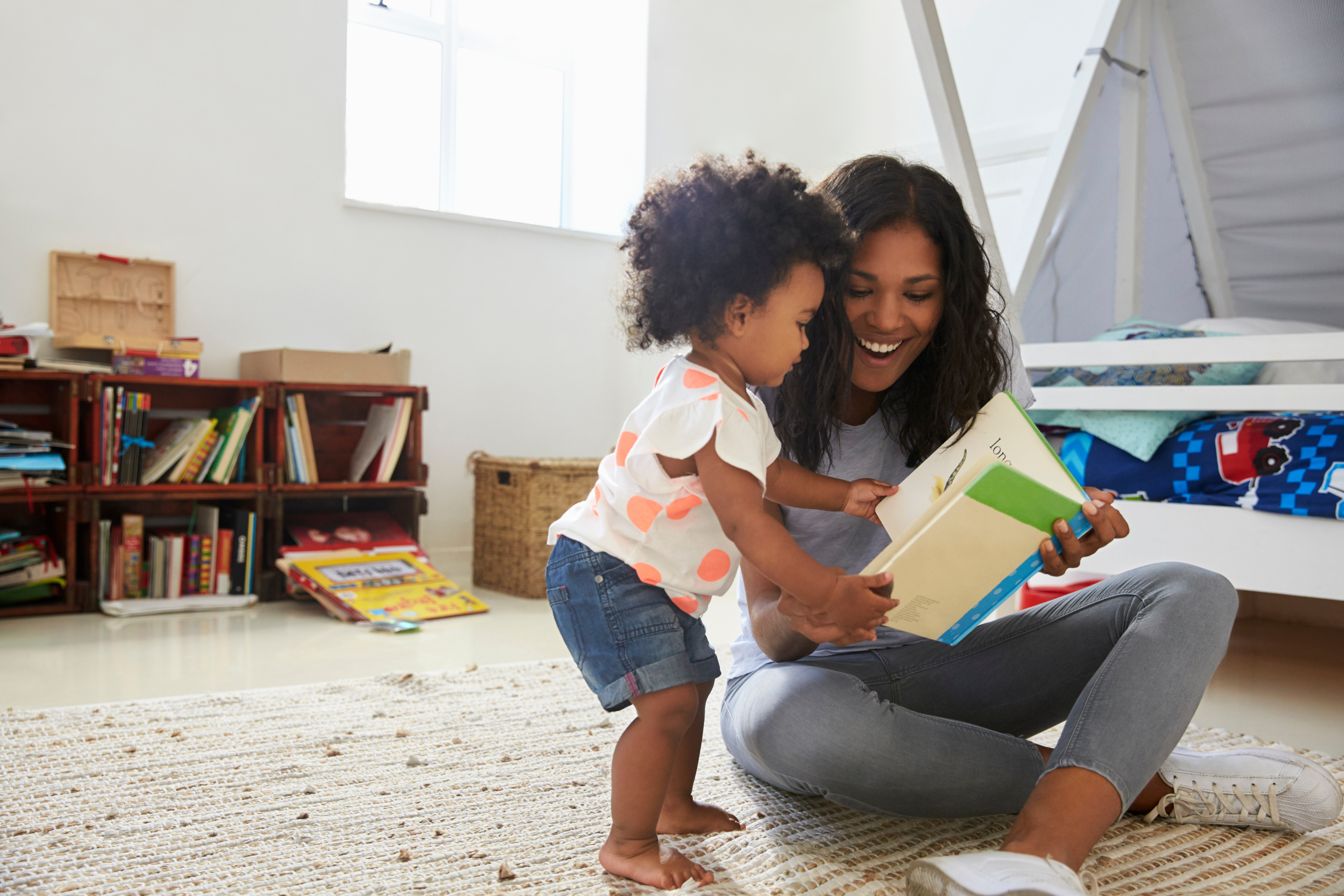 A child and mother read a book together in a play room in their home