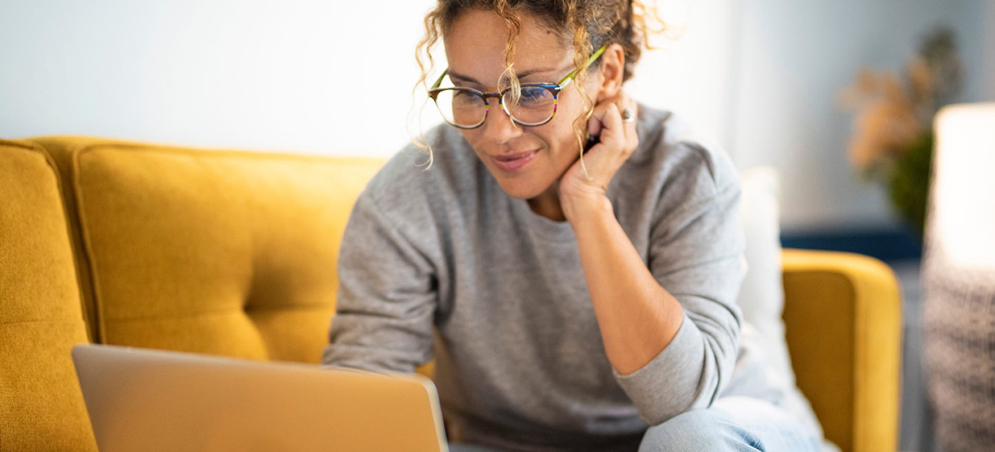 Female sitting on a yellow couch using laptop and internet connection and smile. Happy woman in indoor technology leisure activity. Social media life account concept. Adult Lady writing on computer