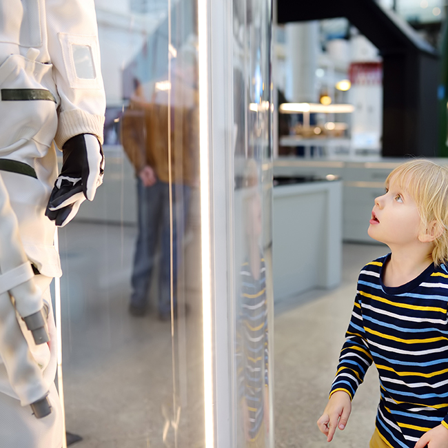 Little blond caucasian boy looking astronaut space suit in museum. Education and entertainment for children. Activities for family with preschooler kids.