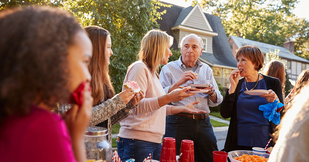 People of all ages enjoy snacks at an outdoor neighborhood meeting.