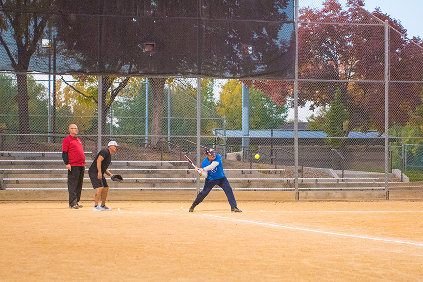 Adult softball player getting ready to swing bat at a ball with umpire and catcher watching.