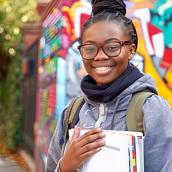 A teenager stands outside with books