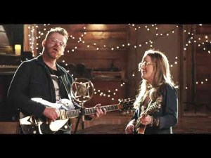 A man and woman with guitars against twinkling lights