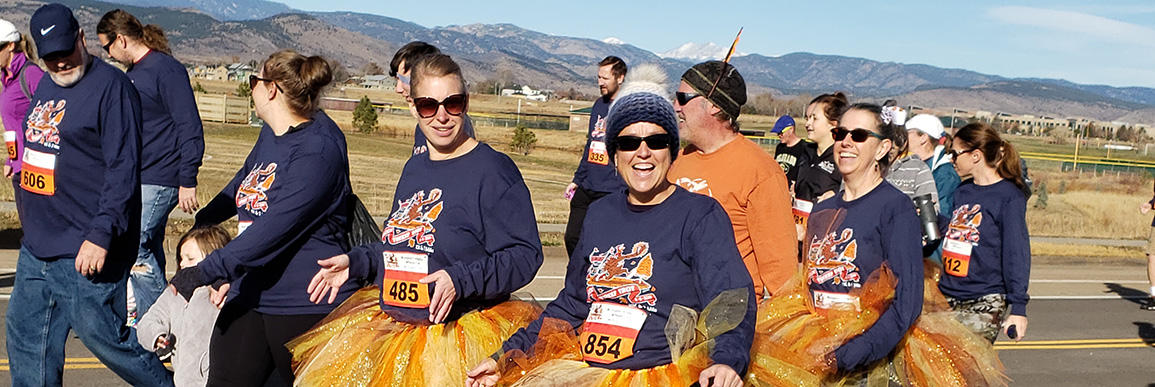 Racers in navy turkey trot event shirts smile as they walk the course with mountains in the background