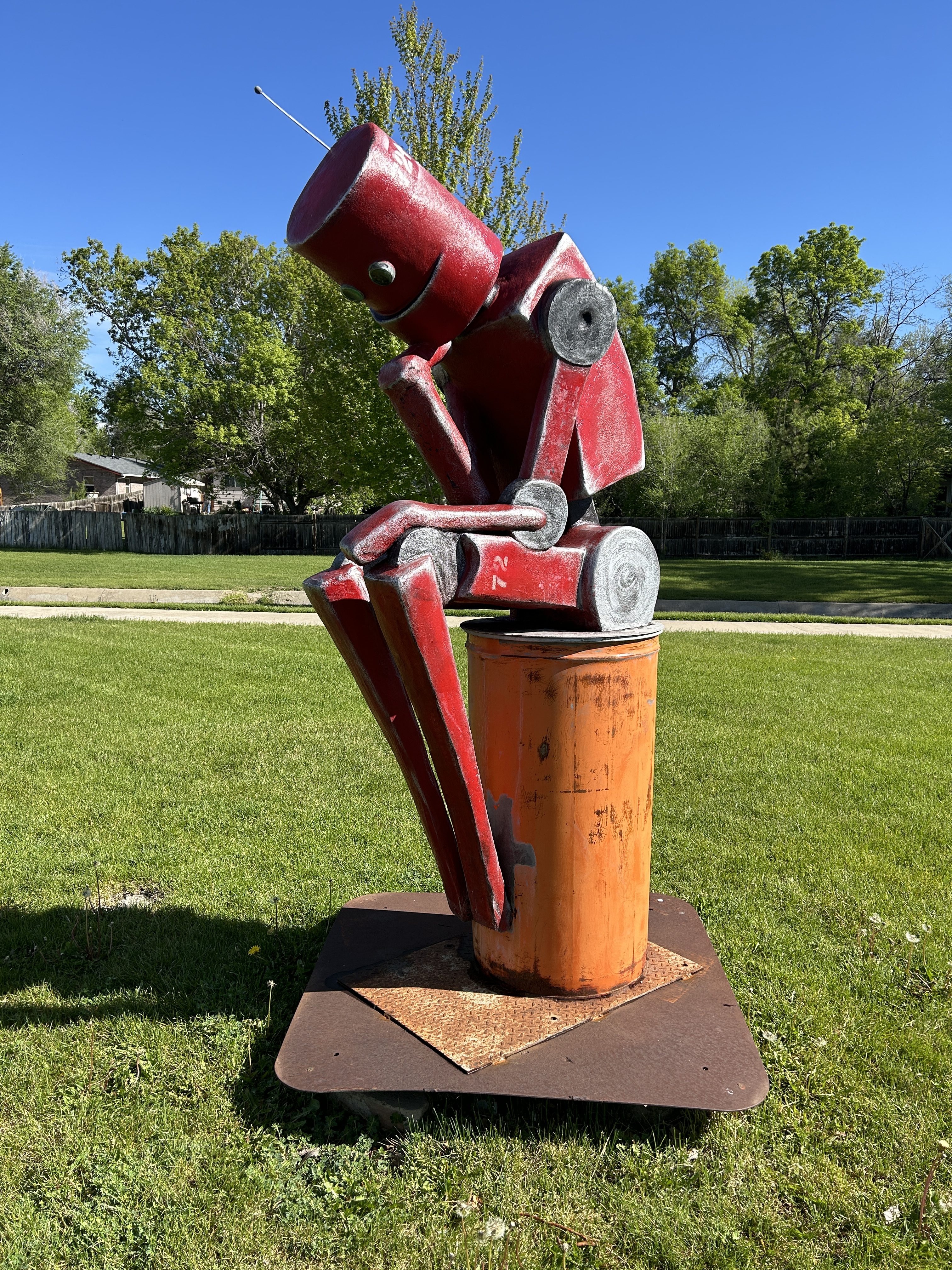 a pensive red robot sitting on an orange drum sculpture