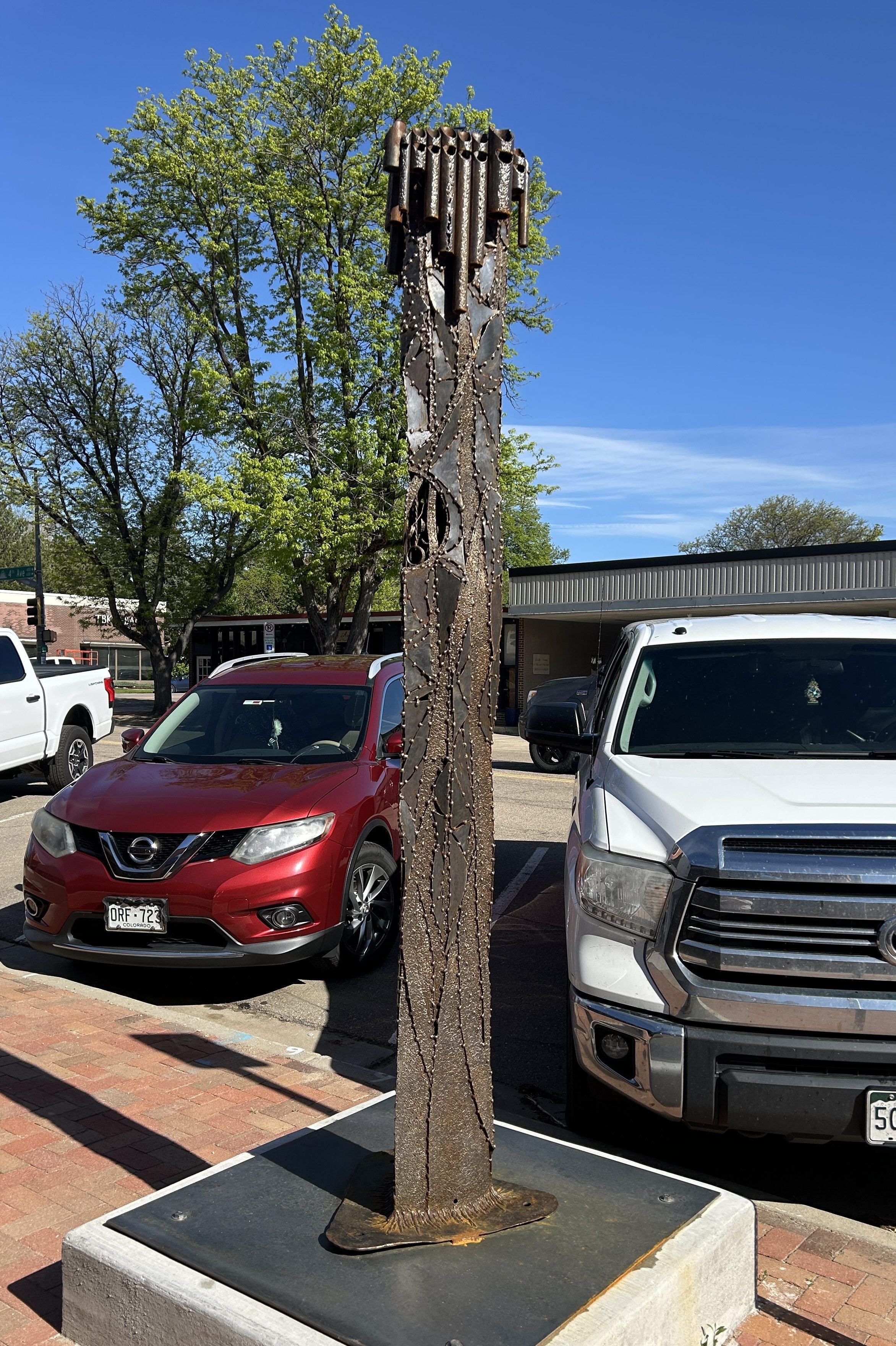 a tall brown triangular abstract steel sculpture on the sidewalk